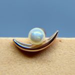 Pearl on a curved silver setting against a blue and beige background