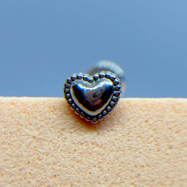 Close-up of a heart-shaped silver stud earring against a blurred blue background