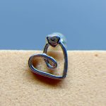 A silver heart-shaped wire earring on a beige surface against a blue background