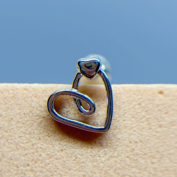 A silver heart-shaped wire earring on a beige surface against a blue background