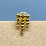 Close-up of a gold beaded earring or jewellery piece against skin, with a blue background