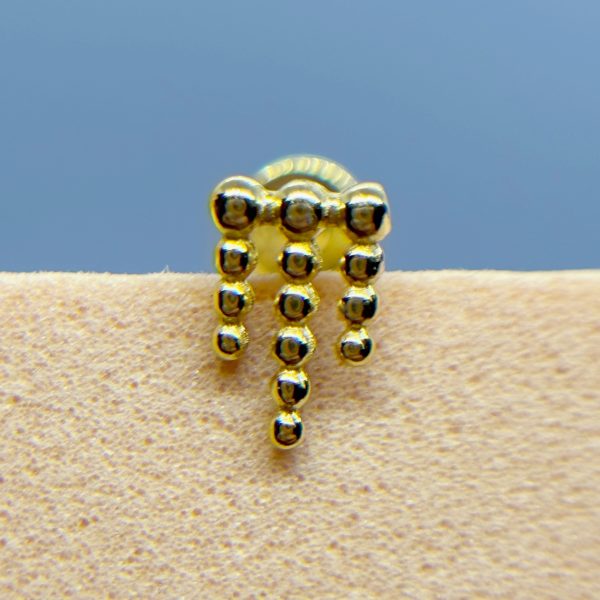 Close-up of a gold beaded earring or jewellery piece against skin, with a blue background
