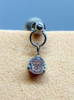 Close-up of a silver earring with a round clear gemstone against a beige background