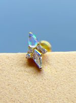 Close-up of a gold earring with iridescent and clear gemstones against a blue background