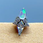 Close-up of a gemstone ear stud with an iridescent teardrop stone and clear crystals on skin