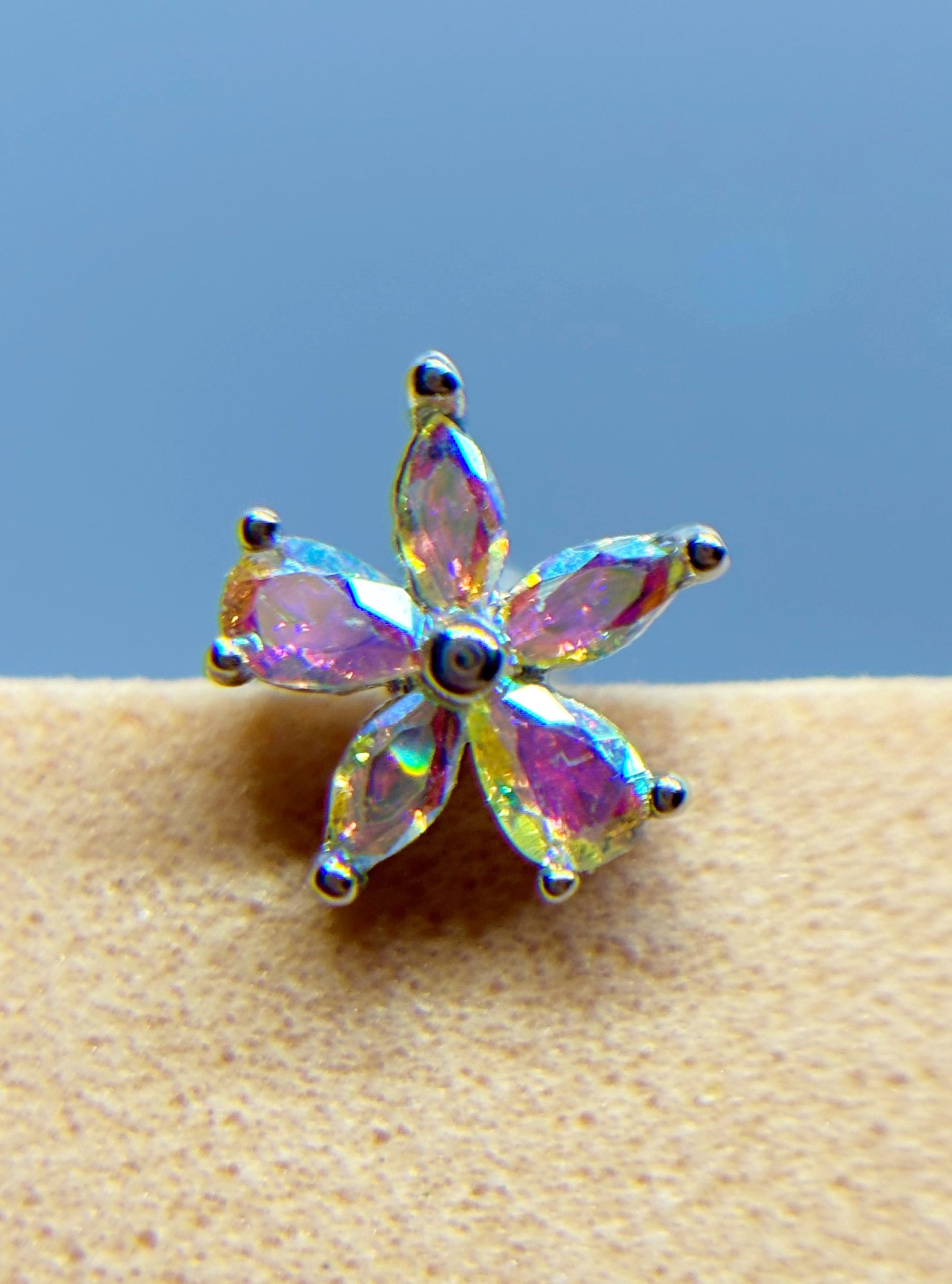 IMG_9432 Close-up of a iridescent crystal flower stud earring against a blue background
