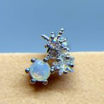 Close-up of a silver ring with an opal stone and crystal flower-like clusters against a blue background