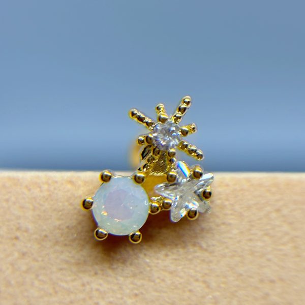 Close-up of three gold stud earrings with clear and opalescent gemstones on skin