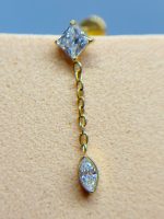 Gold chain earring with two clear gemstone drops against skin on a blue background