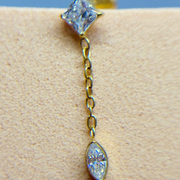 Gold chain earring with two clear gemstone drops against skin on a blue background