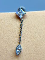 Close-up of a dangling crystal earring with a diamond-shaped stud and teardrop pendant on skin