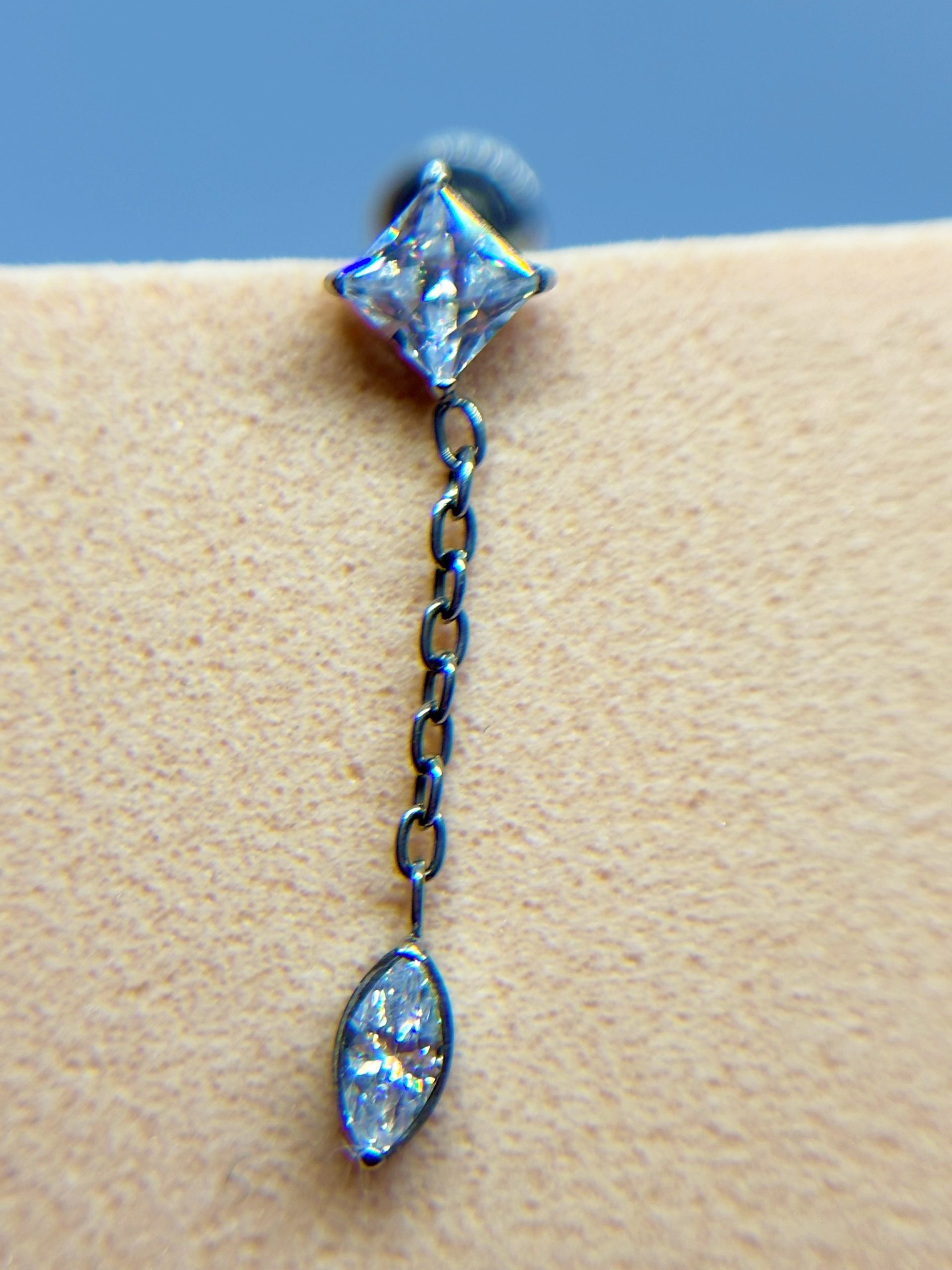 IMG_9437 Close-up of a dangling crystal earring with a diamond-shaped stud and teardrop pendant on skin