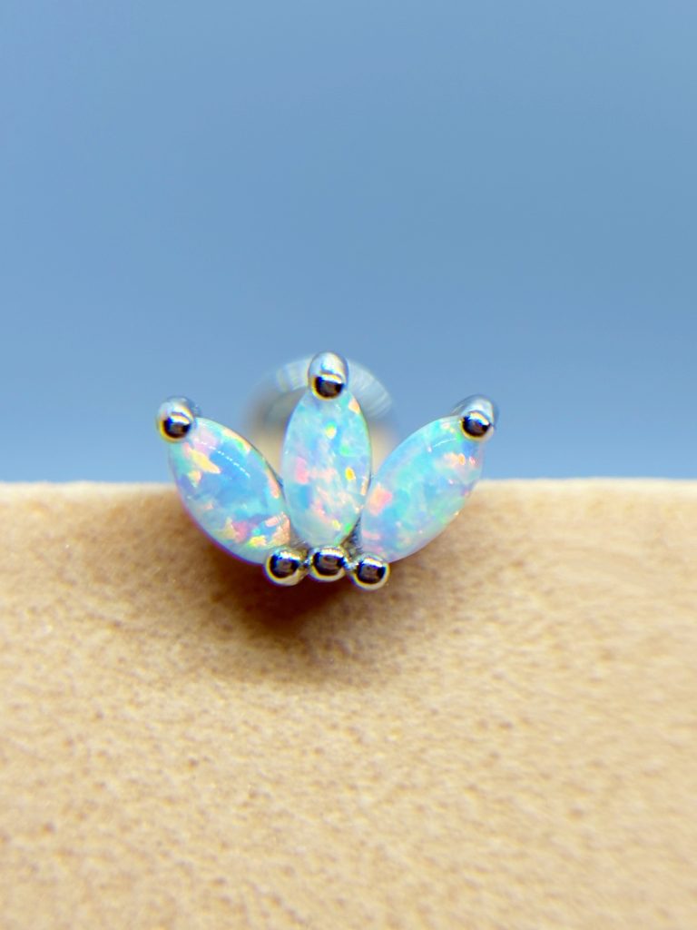 Three opal marquise stones set in a silver stud earring against a blue background