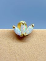 Close-up of an opal flower-shaped nose stud with gold accents against blue sky and skin