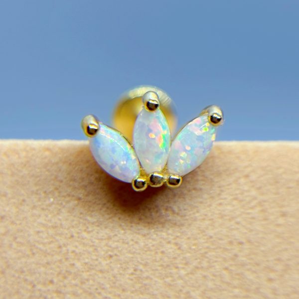 Close-up of an opal flower-shaped nose stud with gold accents against blue sky and skin