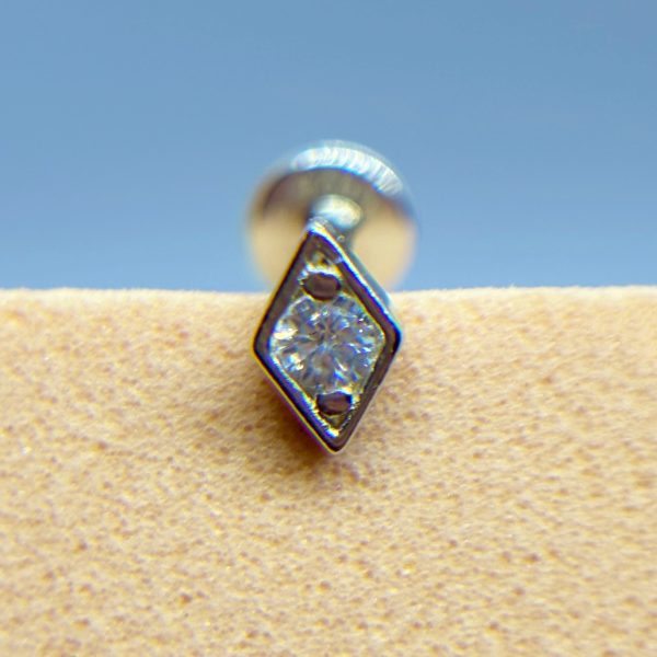Close-up of a diamond-shaped stud earring with a clear stone against a blue background