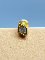 Close-up of a gold stud earring with a clear gem on a beige surface against a blue background
