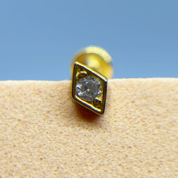 Close-up of a gold stud earring with a clear gem on a beige surface against a blue background