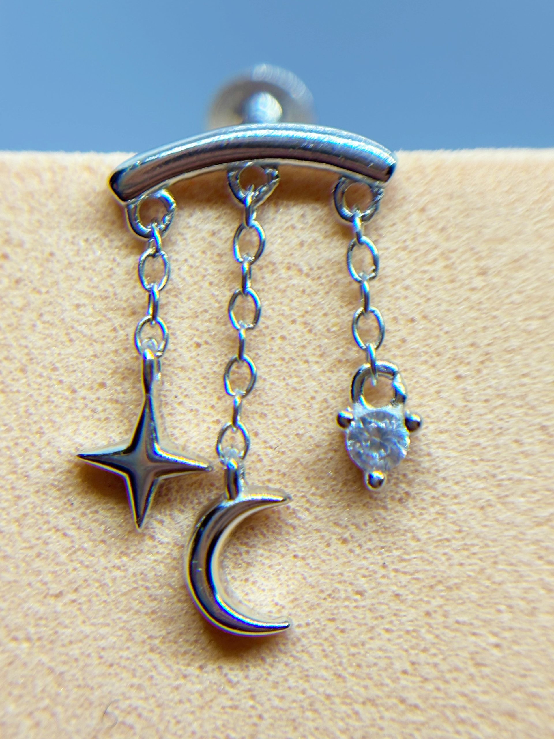 IMG_9443 Silver barbell piercing with three dangling charms: a star, crescent moon and gem set against skin