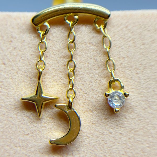 Gold ear cuff with dangling star, crescent moon and gem charms on a beige background
