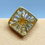 Close-up of a gold and clear gemstone ring with a square setting against a blue background