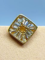 Close-up of a gold and clear gemstone ring with a square setting against a blue background