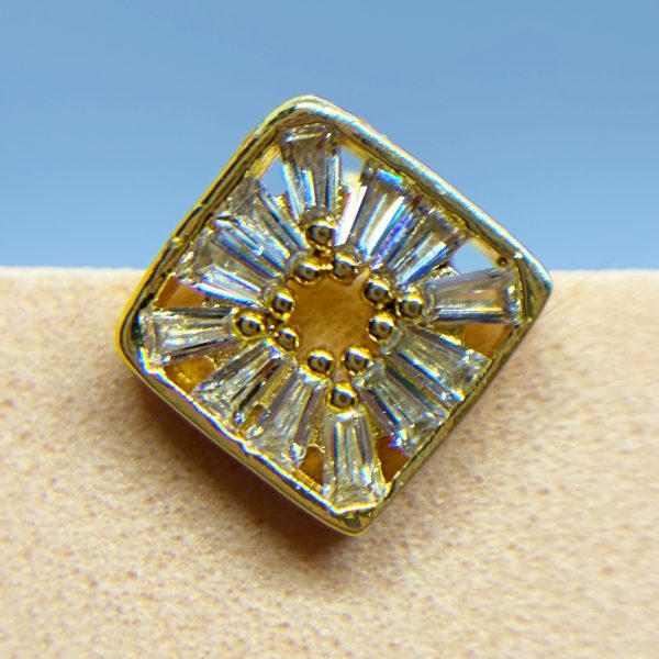 Close-up of a gold and clear gemstone ring with a square setting against a blue background