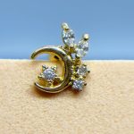Gold crescent moon earring with sparkling clear stones against a blue background