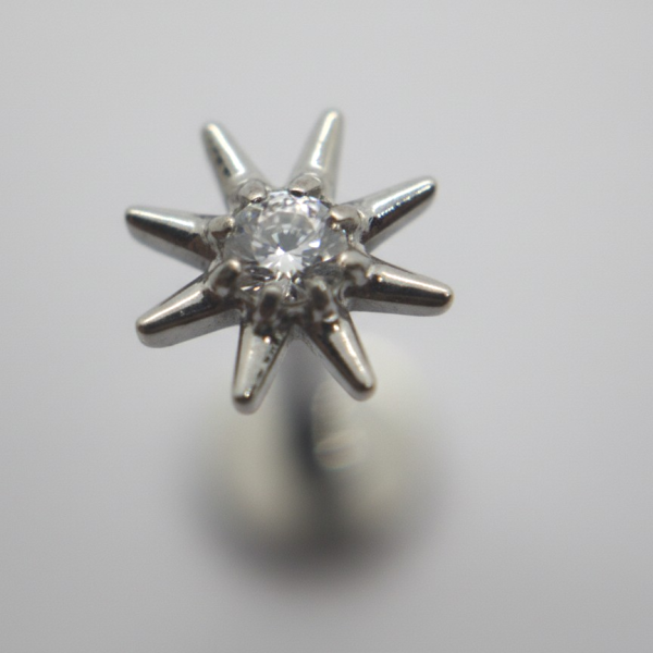 Close-up of an eight-pointed silver star stud with a small central clear gemstone against a soft gray blurred background