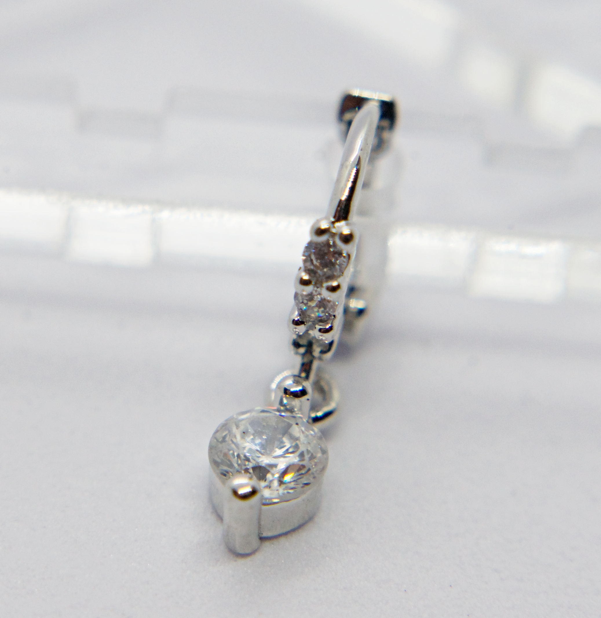 Small silver drop earring with a round clear gemstone and three smaller stones on the hoop above it