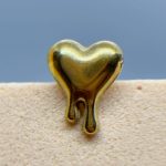 Gold heart-shaped charm against a blue background, resting on a beige textured surface