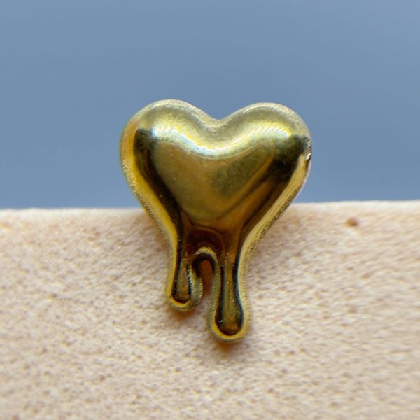 Gold heart-shaped charm against a blue background, resting on a beige textured surface