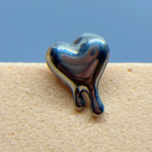 Shiny heart-shaped metal charm on a beige textured surface against a blue background
