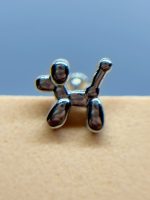 Metal balloon-dog charm on a beige surface against a blue background