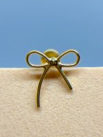 Close-up of a gold bow-shaped earring stud on a beige fabric surface against a blue background