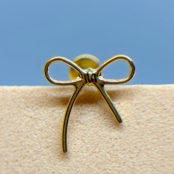 Close-up of a gold bow-shaped earring stud on a beige fabric surface against a blue background