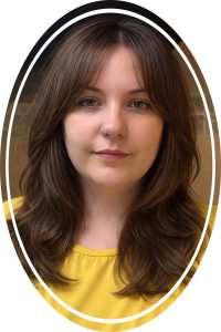 Portrait of a woman with brown hair and a nose ring, wearing a yellow top, framed in an oval